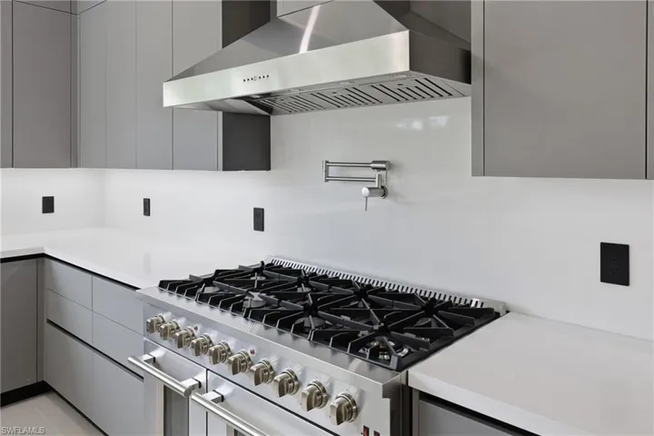 Kitchen view of ventilation hood, double oven range, pot filler, gray cabinets, and modern cabinets