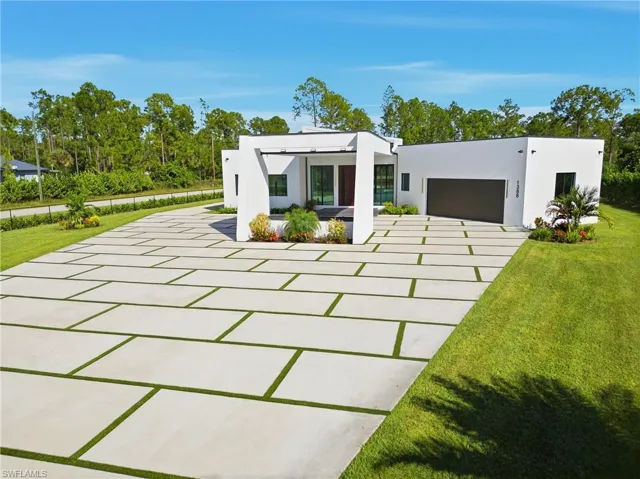 Contemporary home featuring a front lawn, stucco siding, concrete driveway, a patio area, and view of wooded area