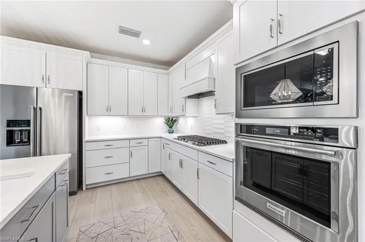 Kitchen with white cabinetry, stainless steel appliances, light stone counters, premium range hood, and light hardwood / wood-style floors
