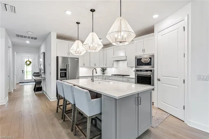 Kitchen featuring stainless steel appliances, a notable chandelier, sink, pendant lighting, and a kitchen island with sink