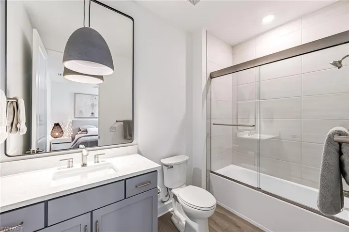 Full bathroom with wood-type flooring, toilet, combined bath / shower with glass door, and vanity