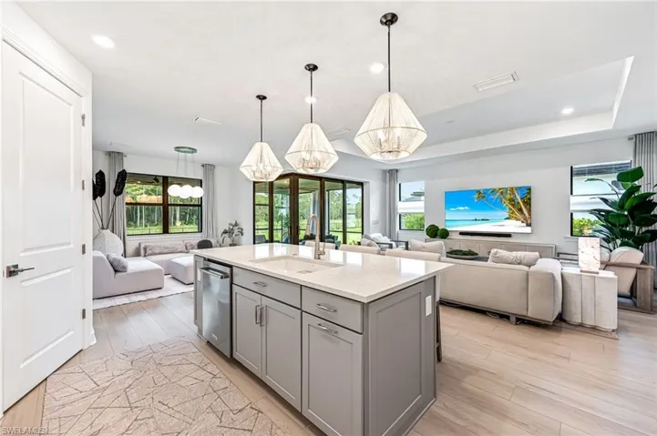 Kitchen with gray cabinetry, light hardwood / wood-style flooring, a chandelier, sink, and a center island with sink