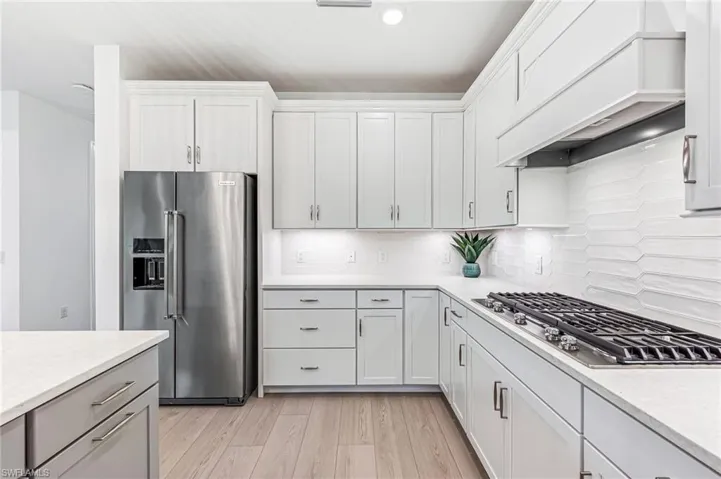 Kitchen with custom exhaust hood, white cabinetry, decorative backsplash, appliances with stainless steel finishes, and light hardwood / wood-style floors
