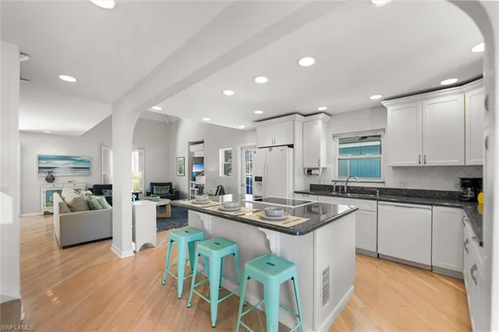 Kitchen featuring arched walkways, a kitchen island, open floor plan, a kitchen bar, and white appliances