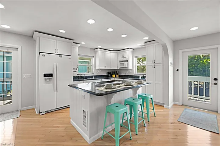 Kitchen with a kitchen breakfast bar, white appliances, a center island, dark stone counters, and light wood finished floors
