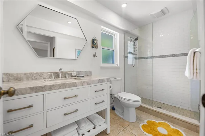 Bathroom with vanity, tiled shower, light tile patterned floors, and recessed lighting