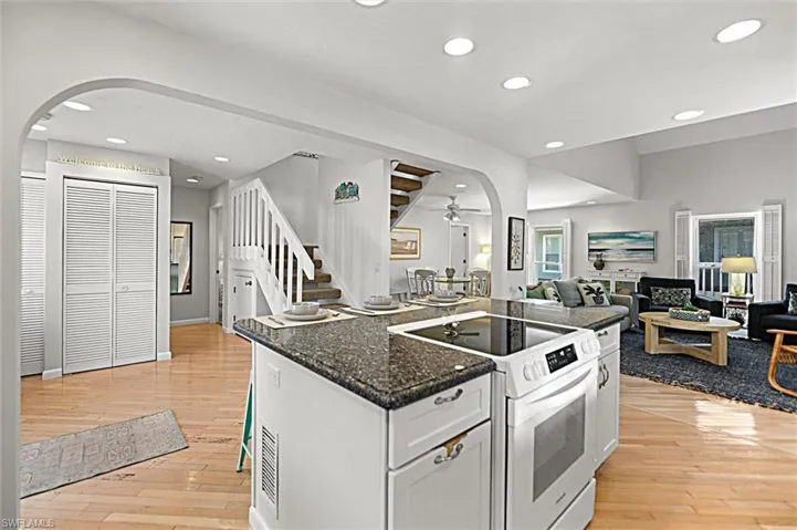 Kitchen with arched walkways, white electric range oven, dark stone counters, open floor plan, and a center island