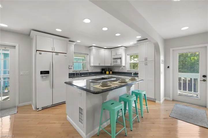 Kitchen featuring white appliances, a breakfast bar, light wood-type flooring, white cabinetry, and recessed lighting