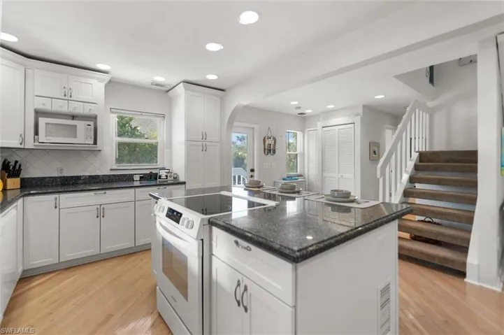 Kitchen featuring white cabinetry, white appliances, dark stone countertops, arched walkways, and a kitchen island