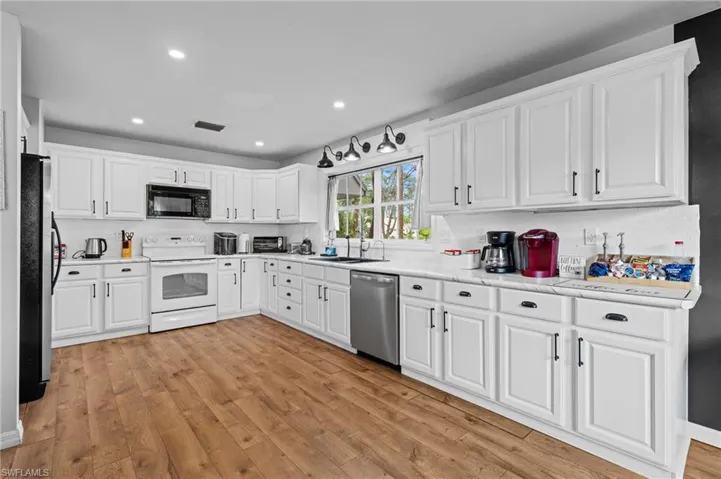 Kitchen featuring a sink, light wood-style floors, backsplash, white cabinets, and appliances with stainless steel finishes