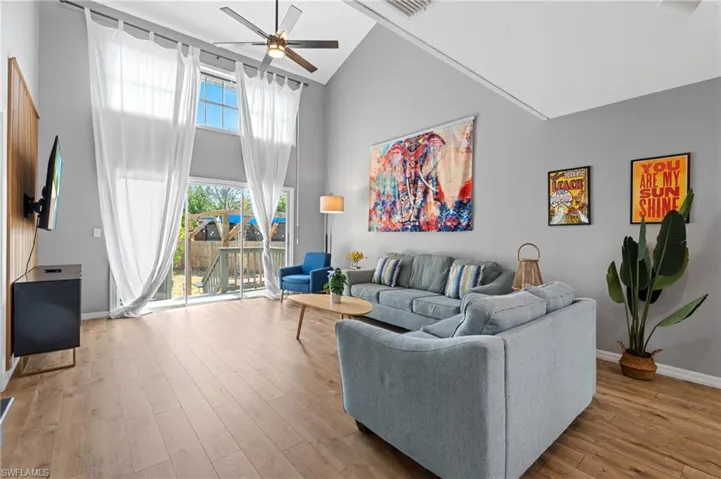 Living area featuring visible vents, ceiling fan, baseboards, wood finished floors, and high vaulted ceiling