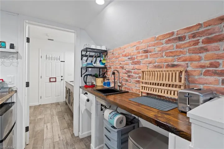 Kitchen with wood counters, a sink, light wood-style floors, brick wall, and vaulted ceiling