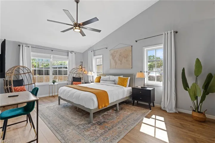 Bedroom with light wood-style floors, baseboards, high vaulted ceiling, and multiple windows