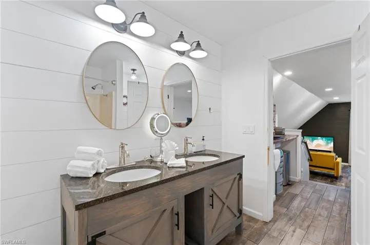 Bathroom with double vanity, a sink, vaulted ceiling, and wood finished floors