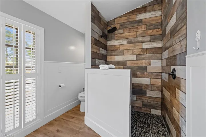 Bathroom with tiled shower, wood finished floors, wainscoting, toilet, and lofted ceiling