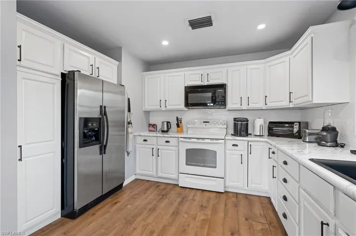 Kitchen featuring white cabinetry, black microwave, visible vents, white electric stove, and stainless steel refrigerator with ice dispenser