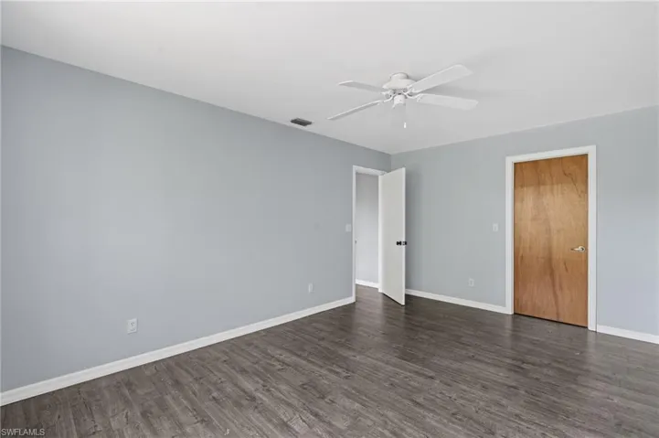 Spare room with a ceiling fan, visible vents, baseboards, and dark wood finished floors