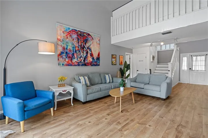 Living room featuring light wood finished floors, rail lighting, stairs, visible vents, and a towering ceiling