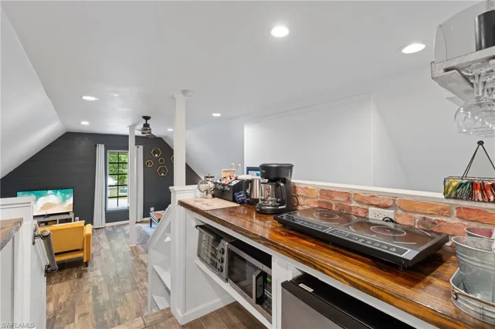 Kitchen with stainless steel microwave, wood counters, vaulted ceiling, white cabinets, and wood finished floors
