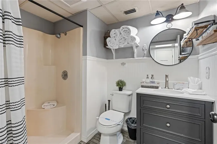 Bathroom featuring curtained shower, visible vents, a wainscoted wall, toilet, and vanity
