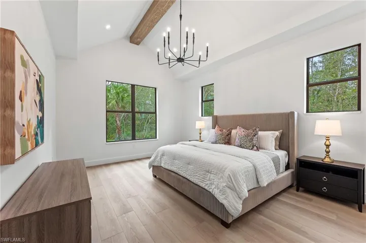 Bedroom with lofted ceiling with beams, light hardwood / wood-style flooring, a notable chandelier, and multiple windows