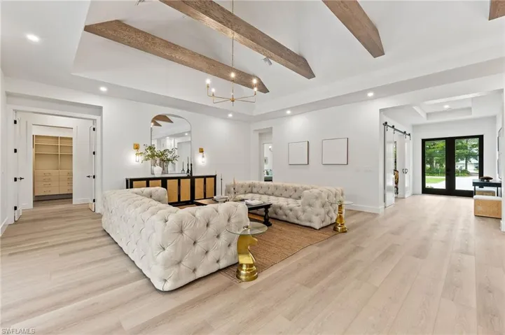 Living room featuring french doors, a barn door, a chandelier, beam ceiling, and light hardwood / wood-style flooring
