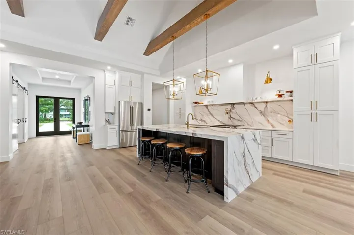 Kitchen with mitered porcelain counters, hanging light fixtures, a barn door, white cabinets, and light wood-type flooring