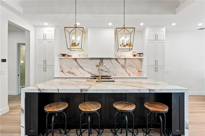 Kitchen with pendant lighting, decorative backsplash, mitered porcelain countertops, white cabinetry, and a large island with sink