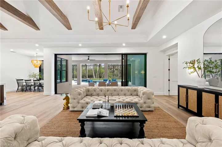 Living room featuring light wood-type flooring, a notable chandelier, and beam ceiling