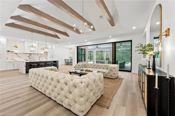 Living room featuring light hardwood / wood-style floors, beamed ceiling, sink, and ceiling fan with notable chandelier