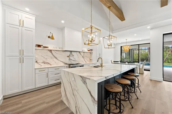 Kitchen with sink, mitered porcelain countertops, a kitchen island with sink, white cabinets, and pendant lighting