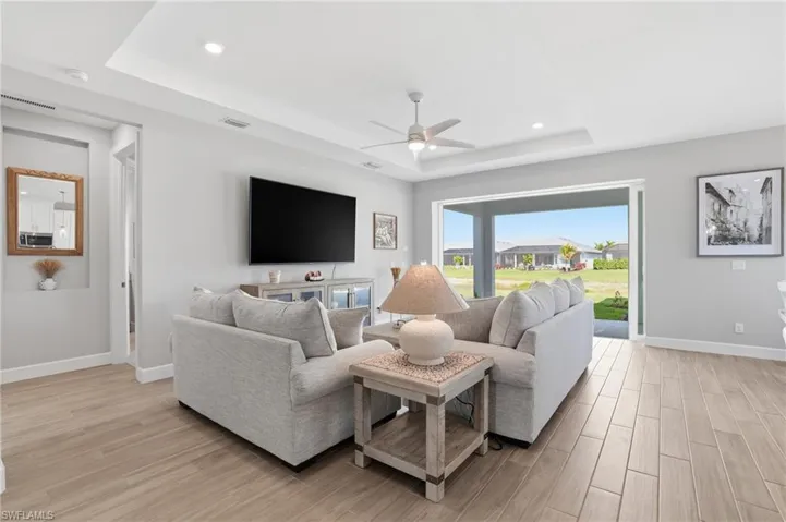 Living area featuring a tray ceiling, light wood-type flooring, ceiling fan, and recessed lighting