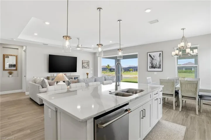 Kitchen with white cabinetry, stainless steel dishwasher, a center island with sink, light wood-style floors, and light stone counters