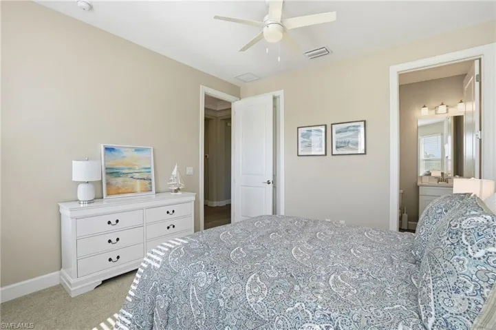 Bedroom with light colored carpet, ceiling fan, and ensuite bathroom
