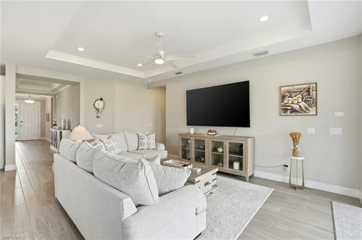 Living room featuring a tray ceiling, wood finish floors, ceiling fan, and recessed lighting