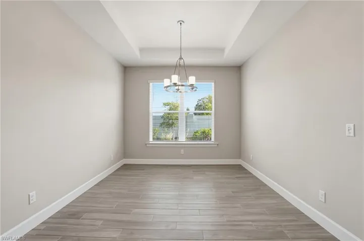 Unfurnished dining area with wood tiled floors, a chandelier, and a tray ceiling