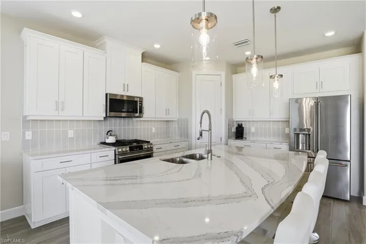 Kitchen with high quality appliances, light stone countertops, white cabinets, and recessed lighting