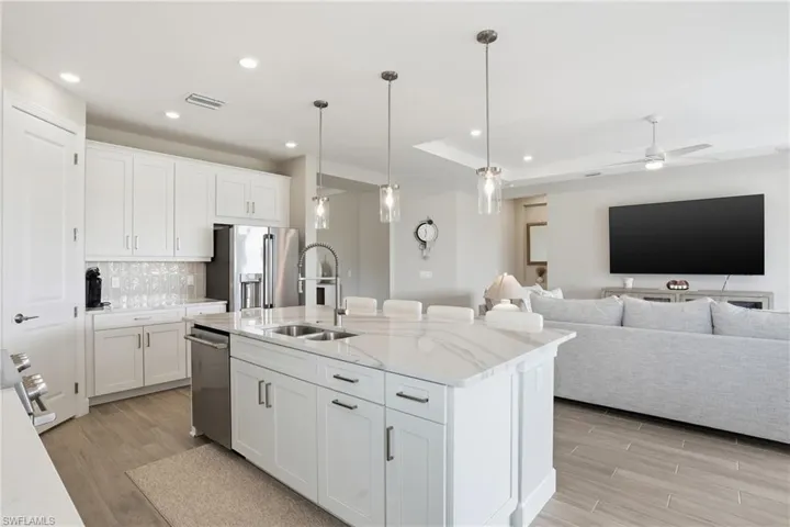 Kitchen featuring white cabinetry, decorative light fixtures, a center island with sink, light stone countertops, and recessed lighting