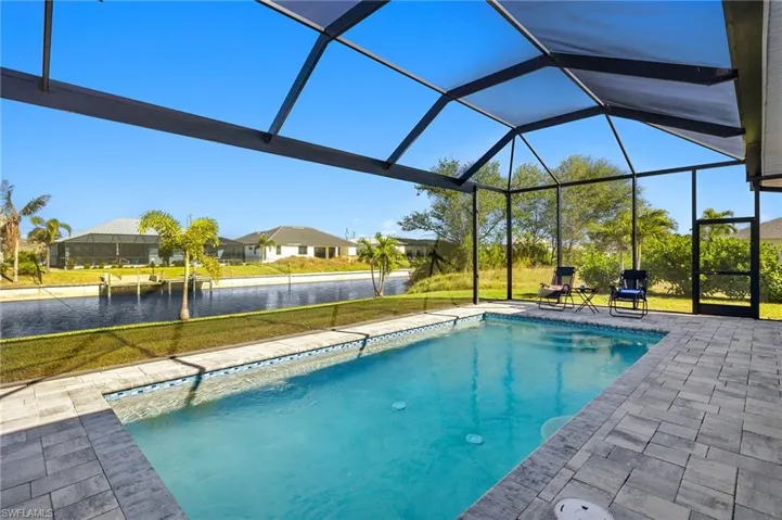 View of pool featuring a yard, a patio, a water view, and glass enclosure