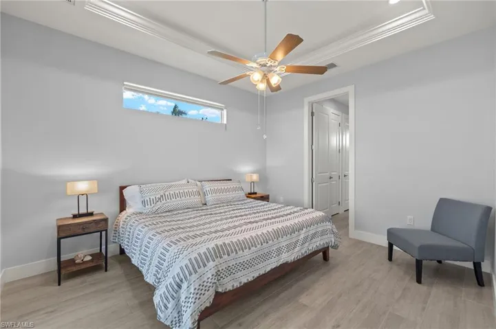 Bedroom with ceiling fan, a raised ceiling, crown molding, and light woodplank tile  flooring