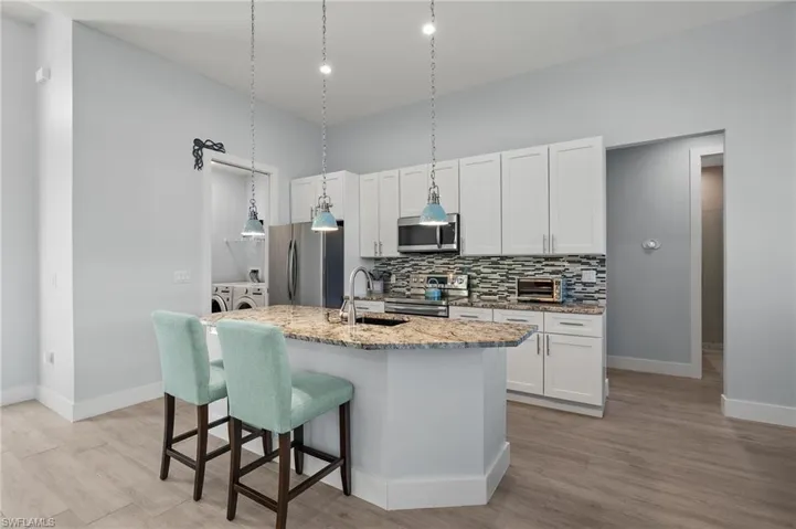 Kitchen featuring light stone countertops, sink, stainless steel appliances, a kitchen island with sink, and washer and clothes dryer