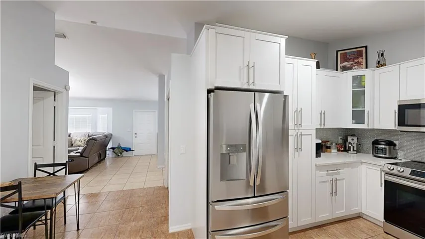 Kitchen with backsplash, light tile patterned floors, appliances with stainless steel finishes, and white cabinets