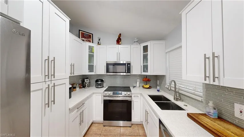 Kitchen with stainless steel appliances, sink, backsplash, and white cabinets
