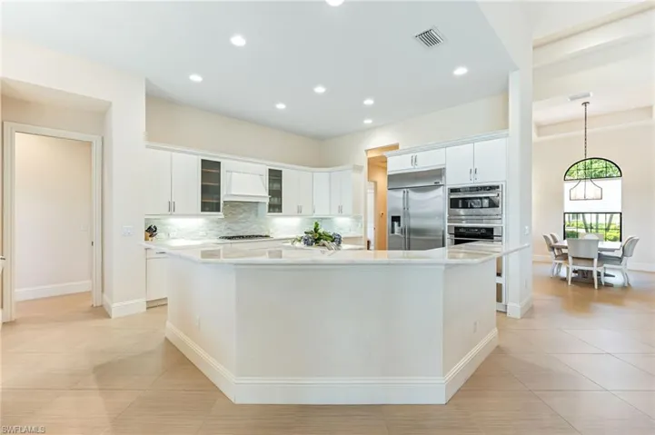 Kitchen featuring tasteful backsplash, glass insert cabinets, appliances with stainless steel finishes, light stone countertops, and white cabinets