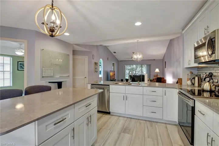 Kitchen featuring quartz counters and island, sink, white cabinetry, vaulted ceiling, and stainless-steel appliances