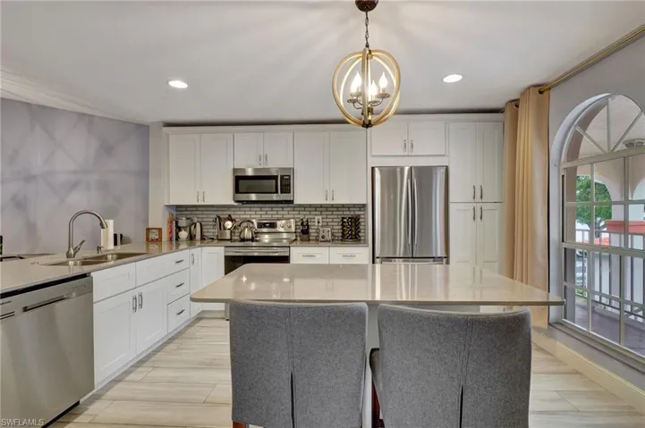 Kitchen with sink, stainless steel appliances, white cabinetry, hanging light fixtures, and glass backsplash