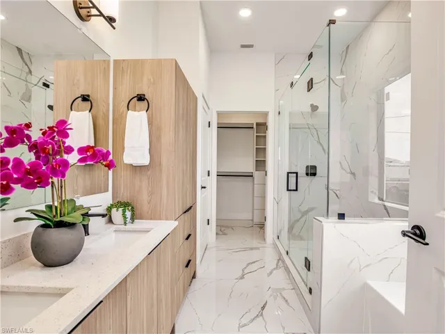 Bathroom featuring a marble style finish shower, marble tiled floors, recessed lighting, a spacious closet, and double vanity