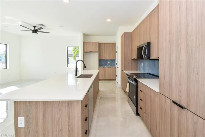Kitchen featuring modern cabinets, appliances with stainless steel finishes, light stone countertops, backsplash, and recessed lighting