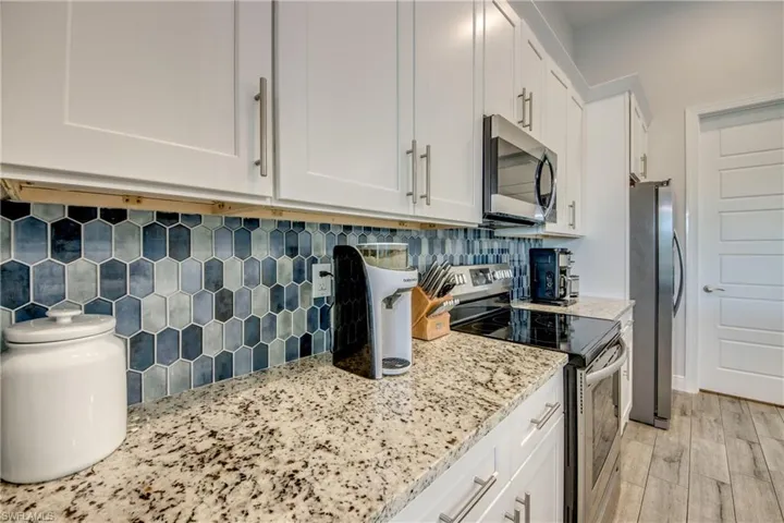 Kitchen featuring stainless steel appliances, white cabinetry, light stone countertops, light wood-style flooring, and tasteful backsplash