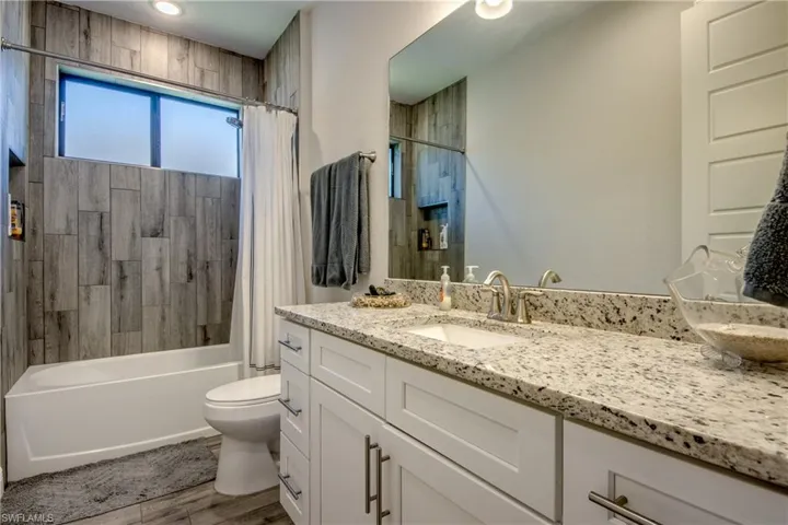 Full bath with toilet, vanity, wood finished floors, and shower / bathtub combination with curtain